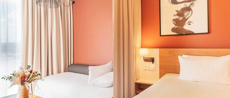 A hotel room with two beds, a wooden nightstand, a vase of flowers, and a painting on the wall.