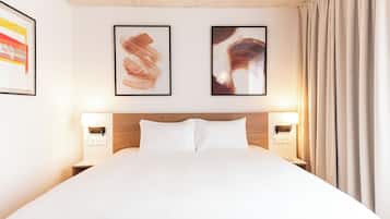 A hotel room with a large bed, two framed artworks on the wall, and a nightstand with a lamp.