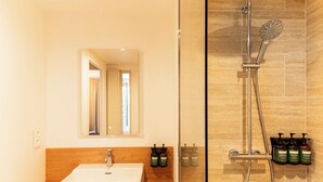 A bathroom with a sink, mirror, shower, and toiletries.