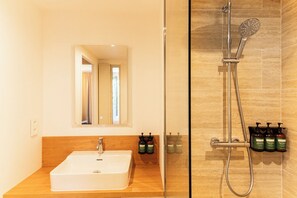 A bathroom with a sink, mirror, shower, and toiletries.