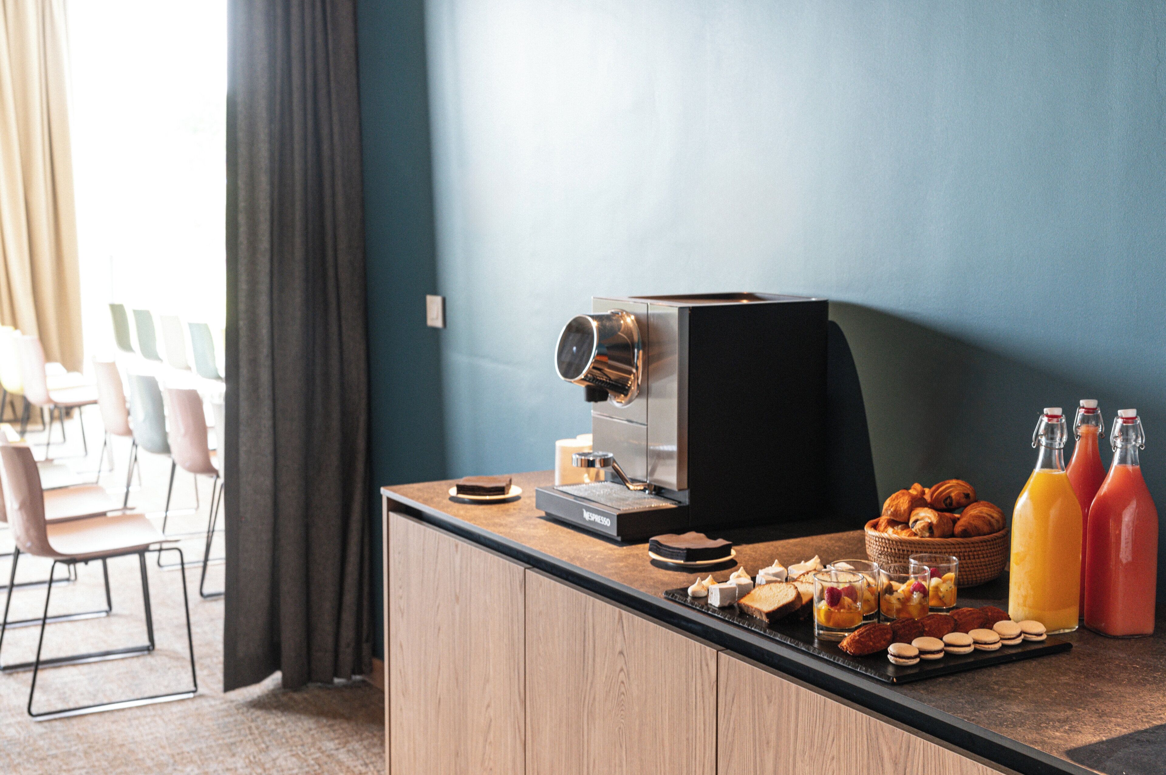 A breakfast setup with a coffee machine, pastries, and juice bottles on a wooden counter.