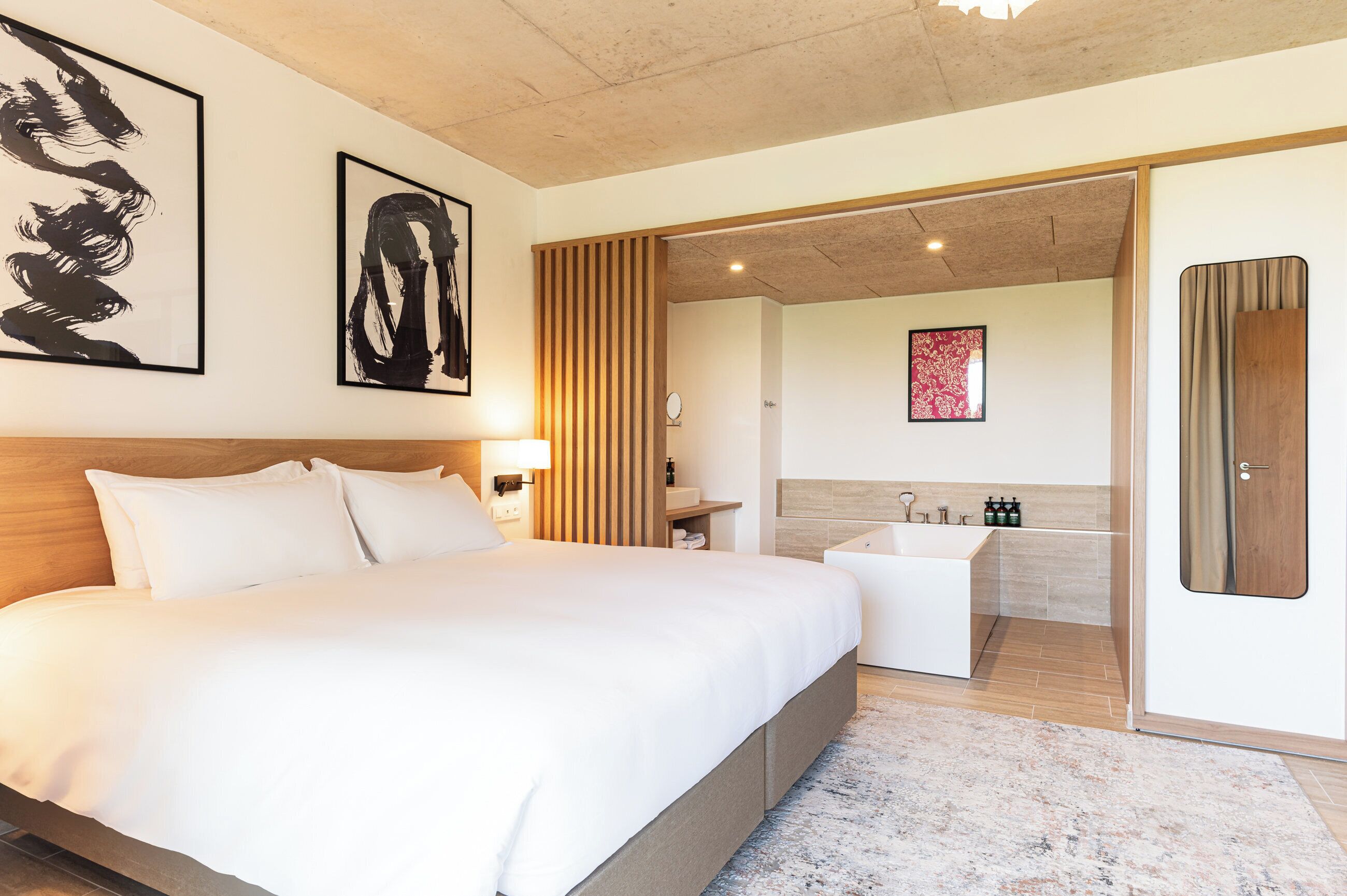 A hotel room with a large bed, a bathroom with a bathtub, and a wooden panel wall.