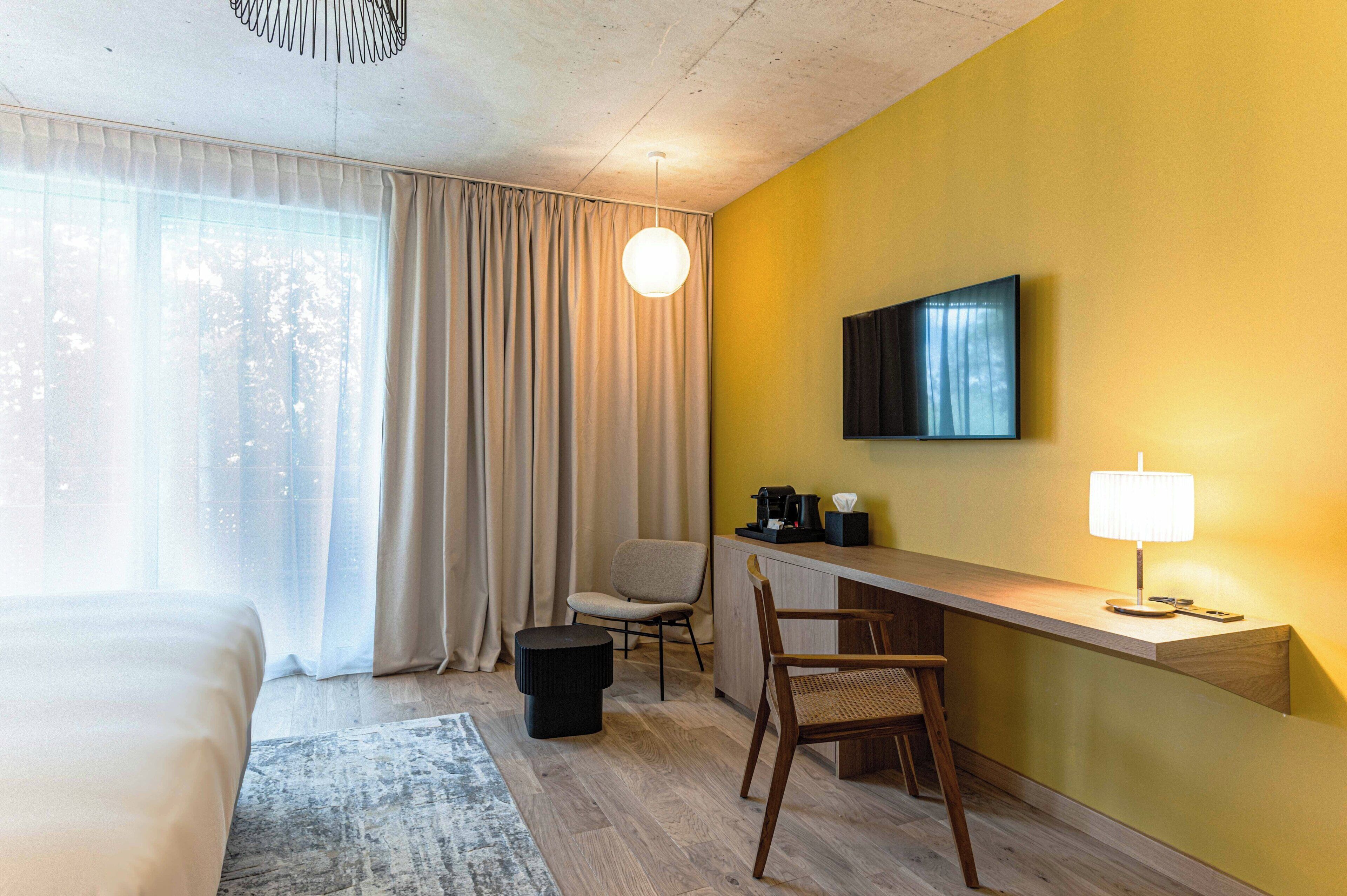 Una habitación de hotel con una cama, un escritorio con silla, televisor y lámpara.