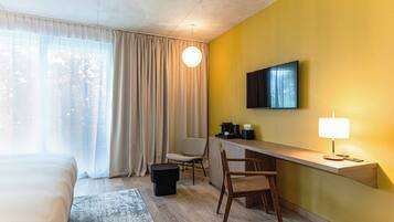 Una habitación de hotel con una cama, un escritorio con silla, televisor y lámpara.