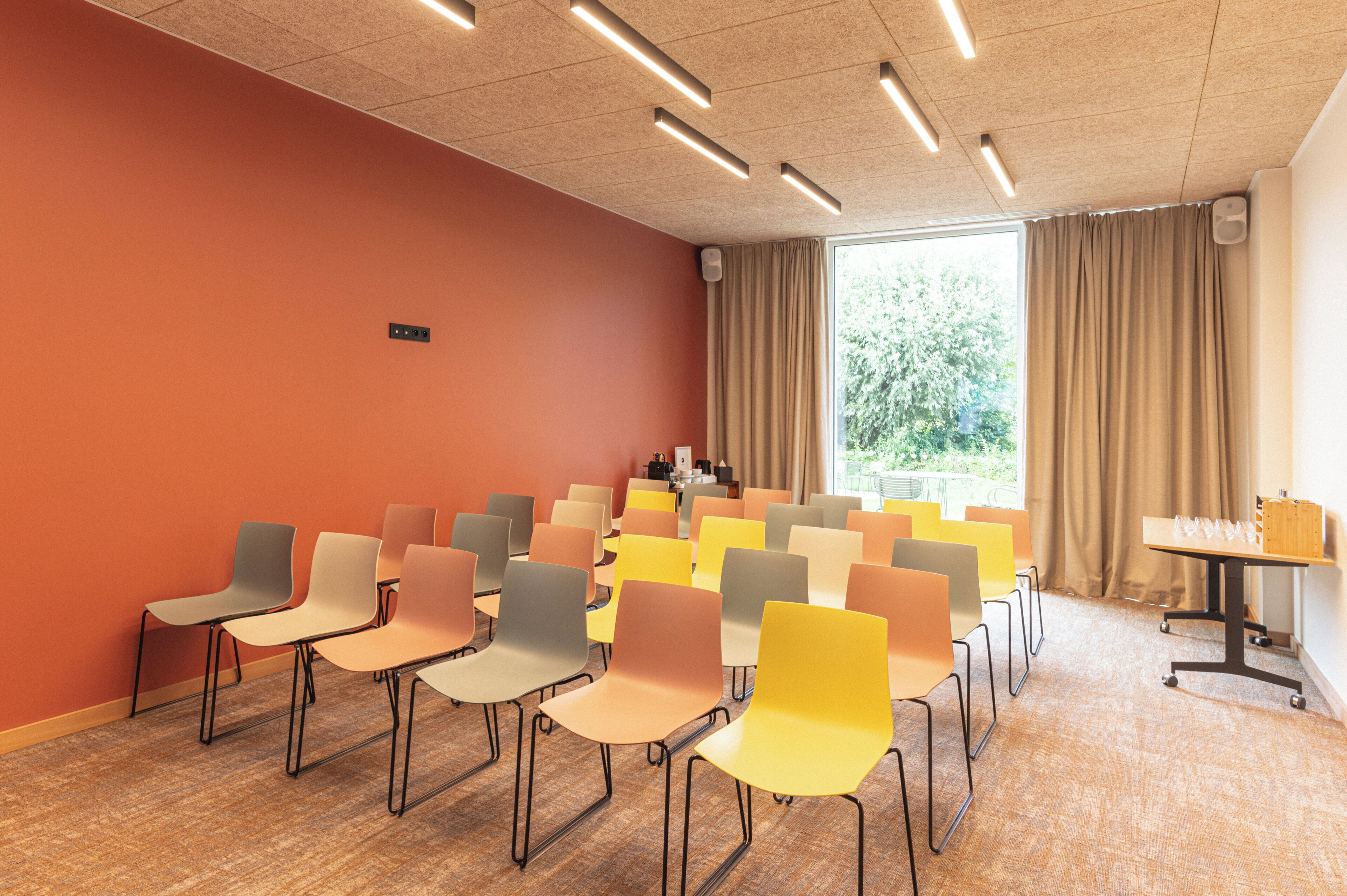 Une salle de conférence avec des rangées de chaises, une table avec des verres et une fenêtre avec des rideaux.