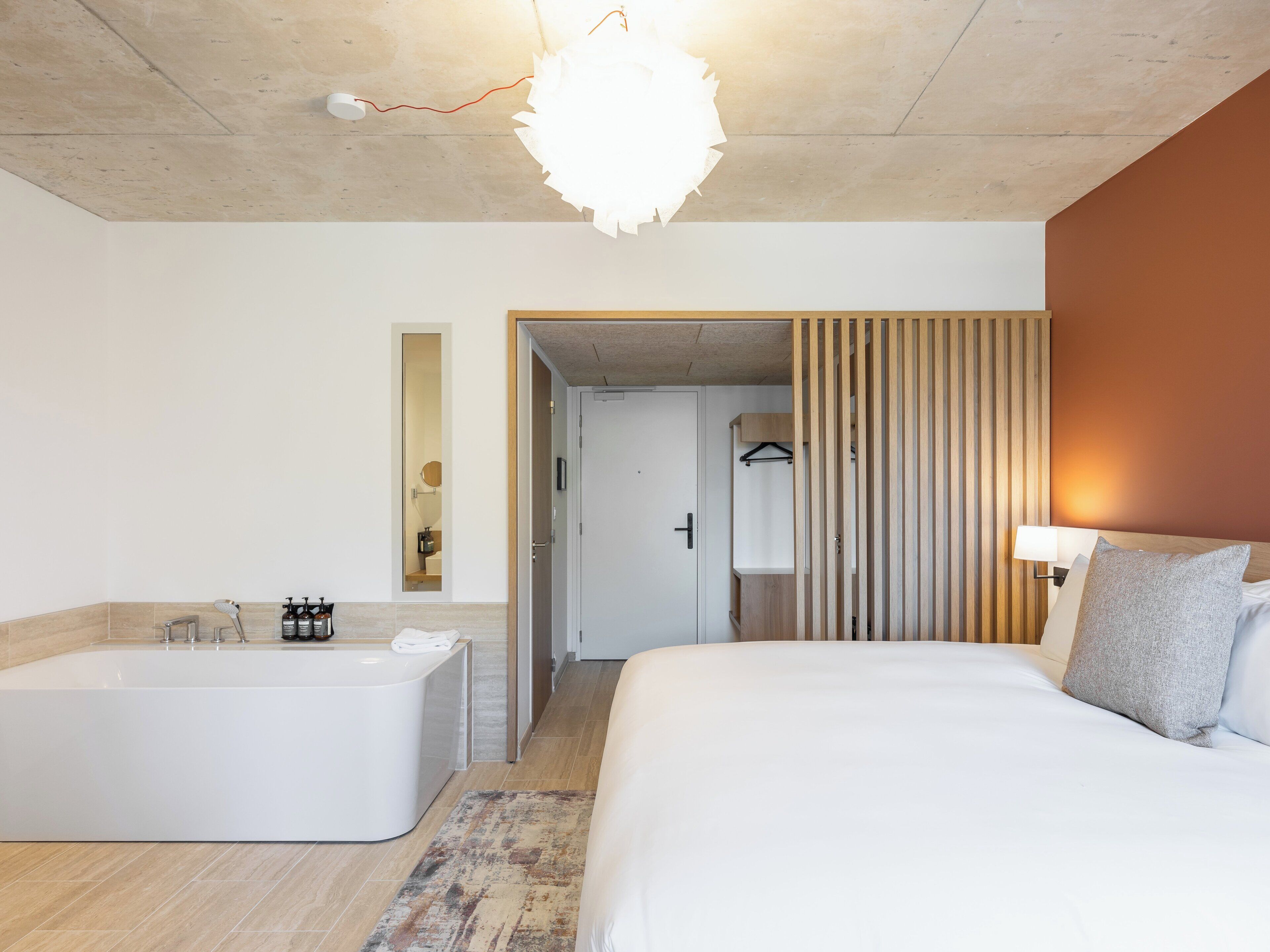 A modern hotel room with a large bed, a separate bathroom with a bathtub, and a wooden panel wall.