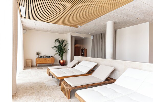A modern spa room with three wooden loungers, a large potted plant, and a minimalist design.