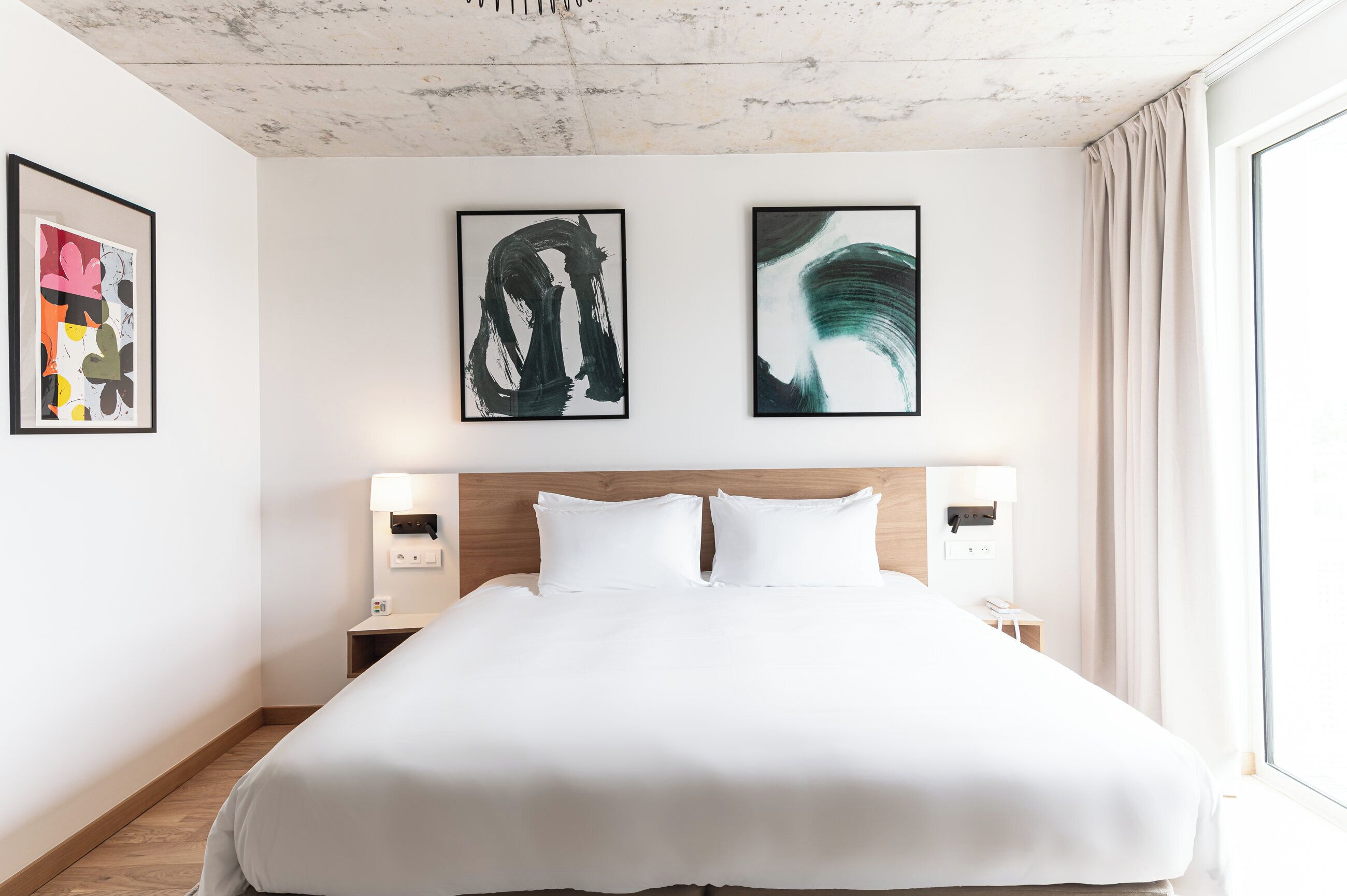 A hotel room with a large bed, two wall-mounted lamps, and abstract art on the walls.