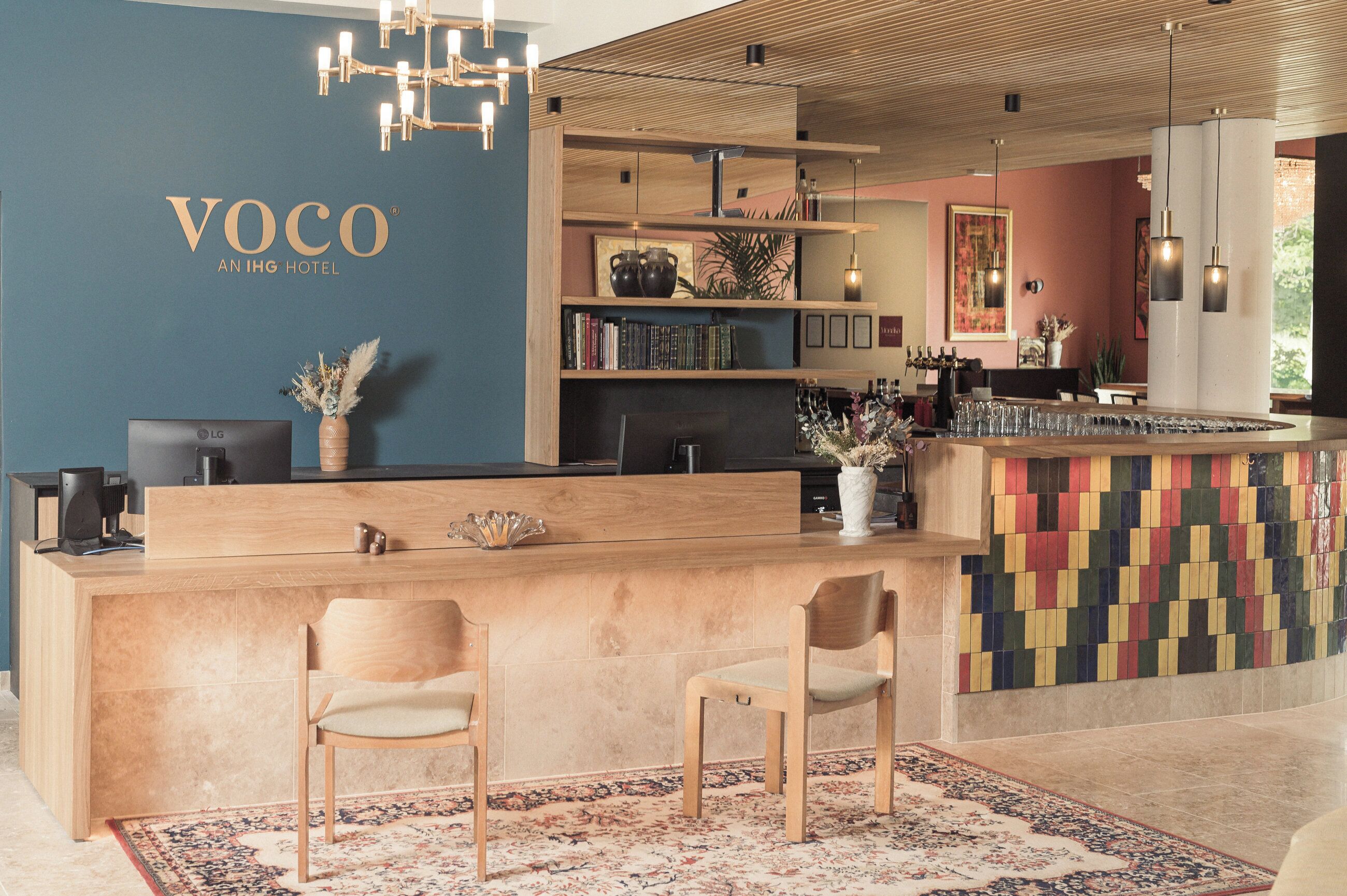 A reception area with a wooden desk, two chairs, a bookshelf, and a colorful tiled wall.