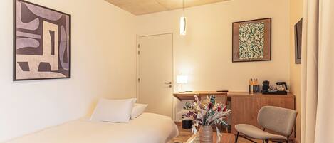 A hotel room with a bed, a desk with a chair, a lamp, and a decorative vase.