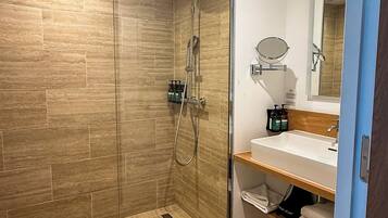 Un baño moderno con ducha envuelta en cristal, tocador con espejo y lavamanos.