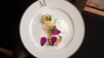 A plate with a dish of food, garnished with green leaves and purple flowers, on a white plate with a red rim.