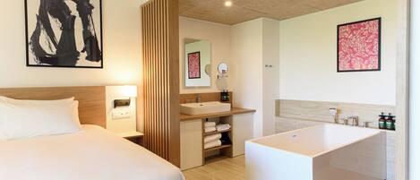 A modern hotel room with a large bed, a separate bathroom with a bathtub, and a wooden partition.