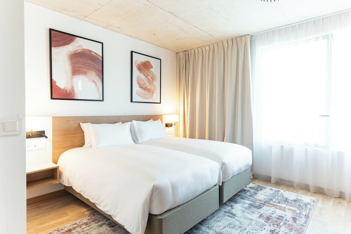 A double bed with a wooden headboard, a bedside table with a lamp, and two abstract paintings on the wall.