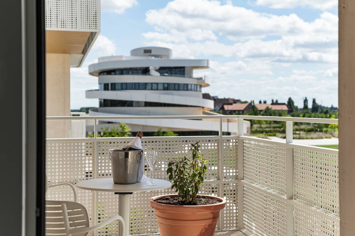 A balcony with a potted plant, a metal bucket, and a glass of water.