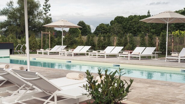 A poolside area with lounge chairs and umbrellas, surrounded by greenery.