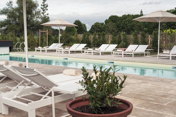 A poolside area with lounge chairs and umbrellas, surrounded by greenery.