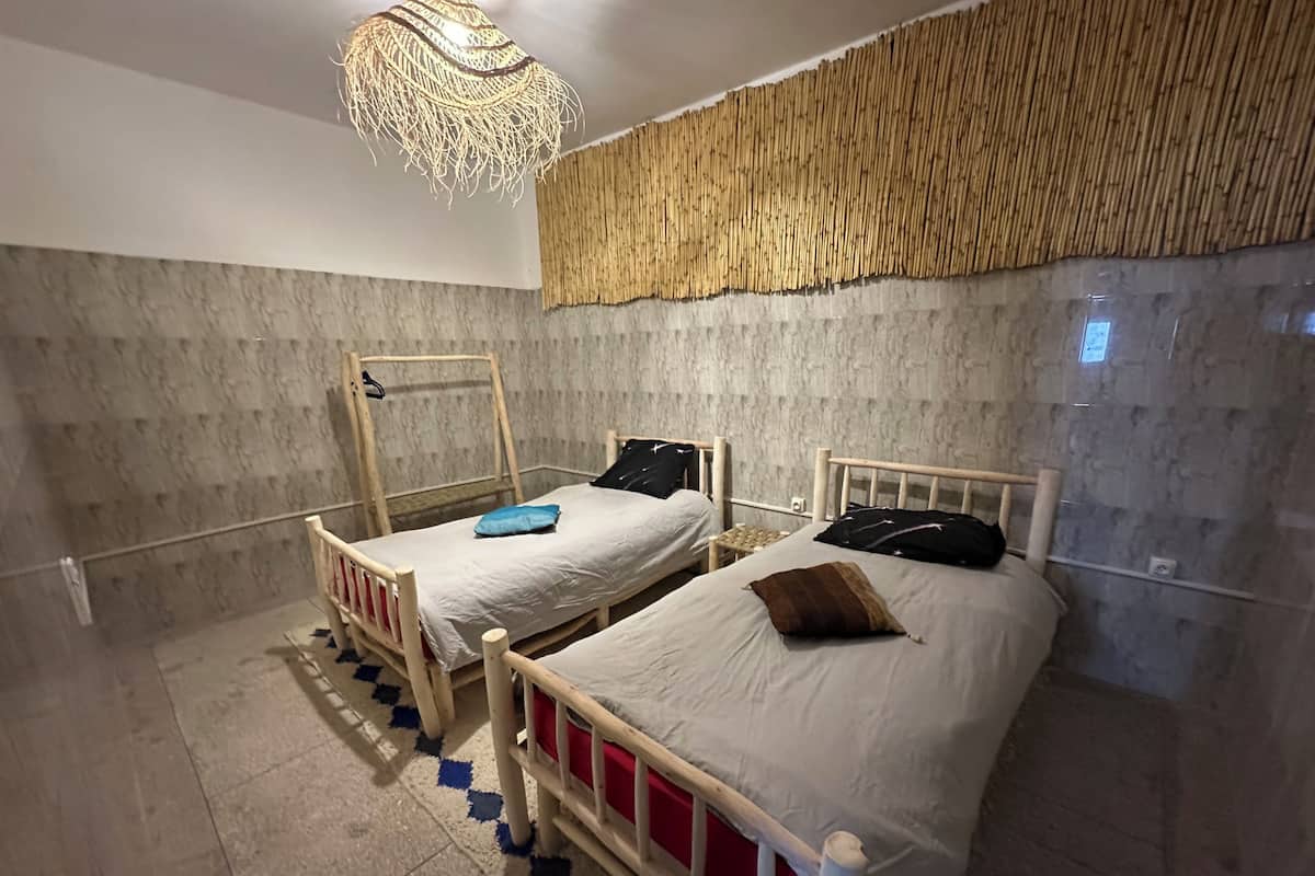 Una habitación con dos camas, una lámpara colgante y una pared con textura.