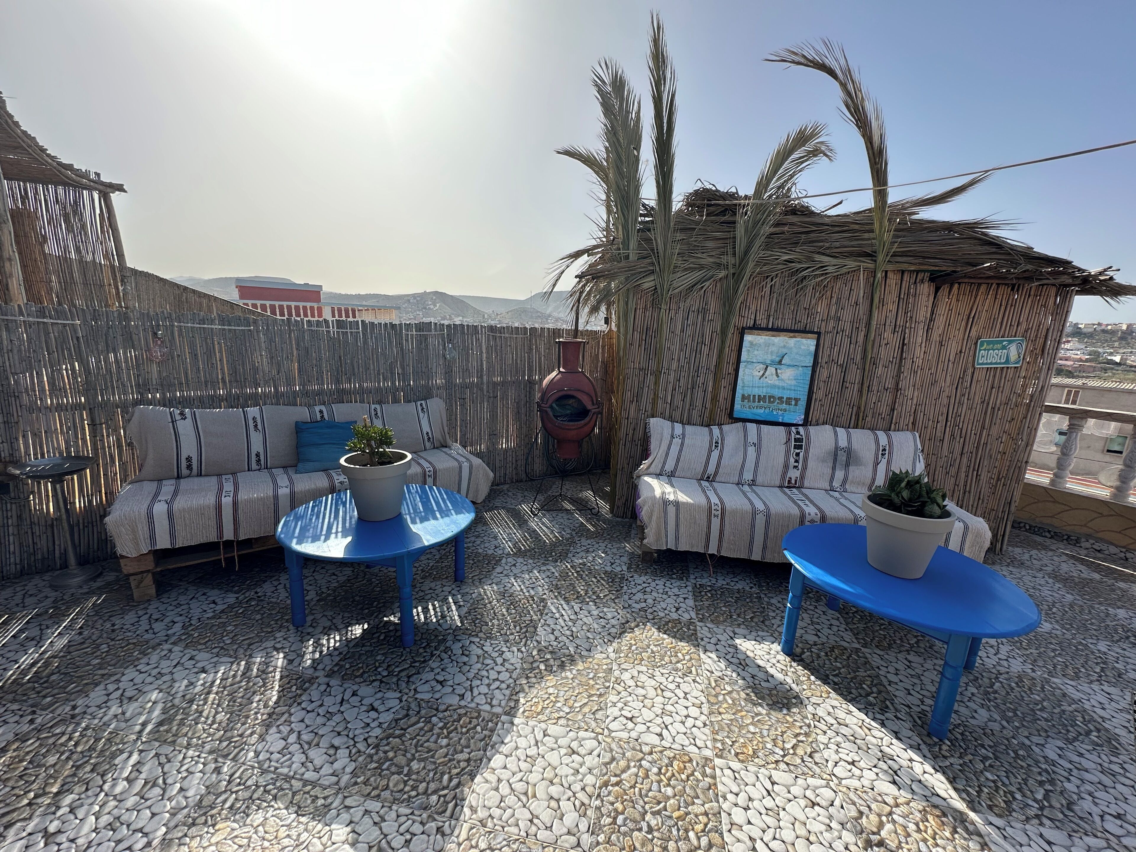 An outdoor seating area with two sofas and two round tables, a bamboo fence, and a view of the city in the background.