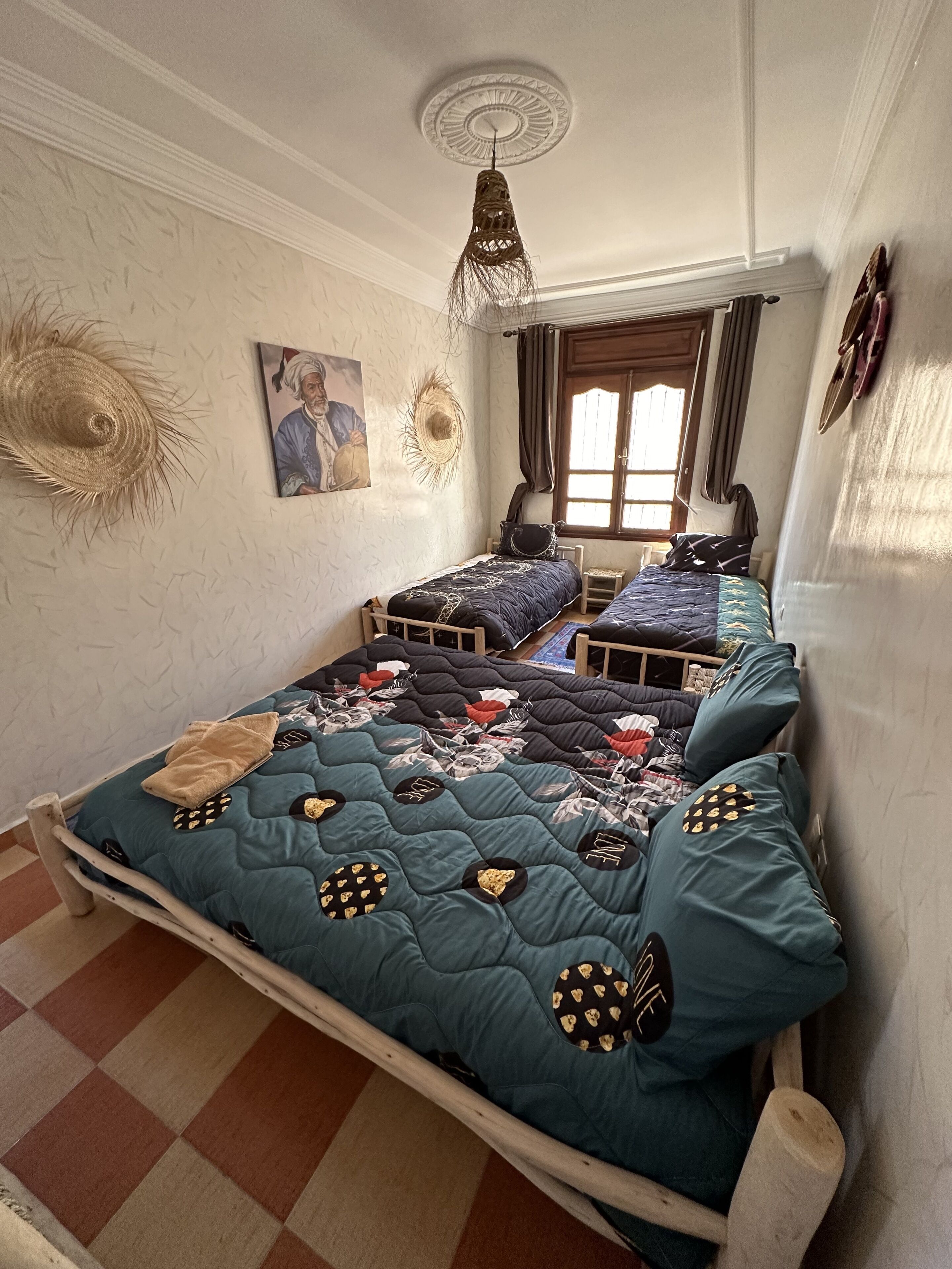 Una habitación con dos camas, un ventilador de techo, un cuadro y una ventana con cortinas.