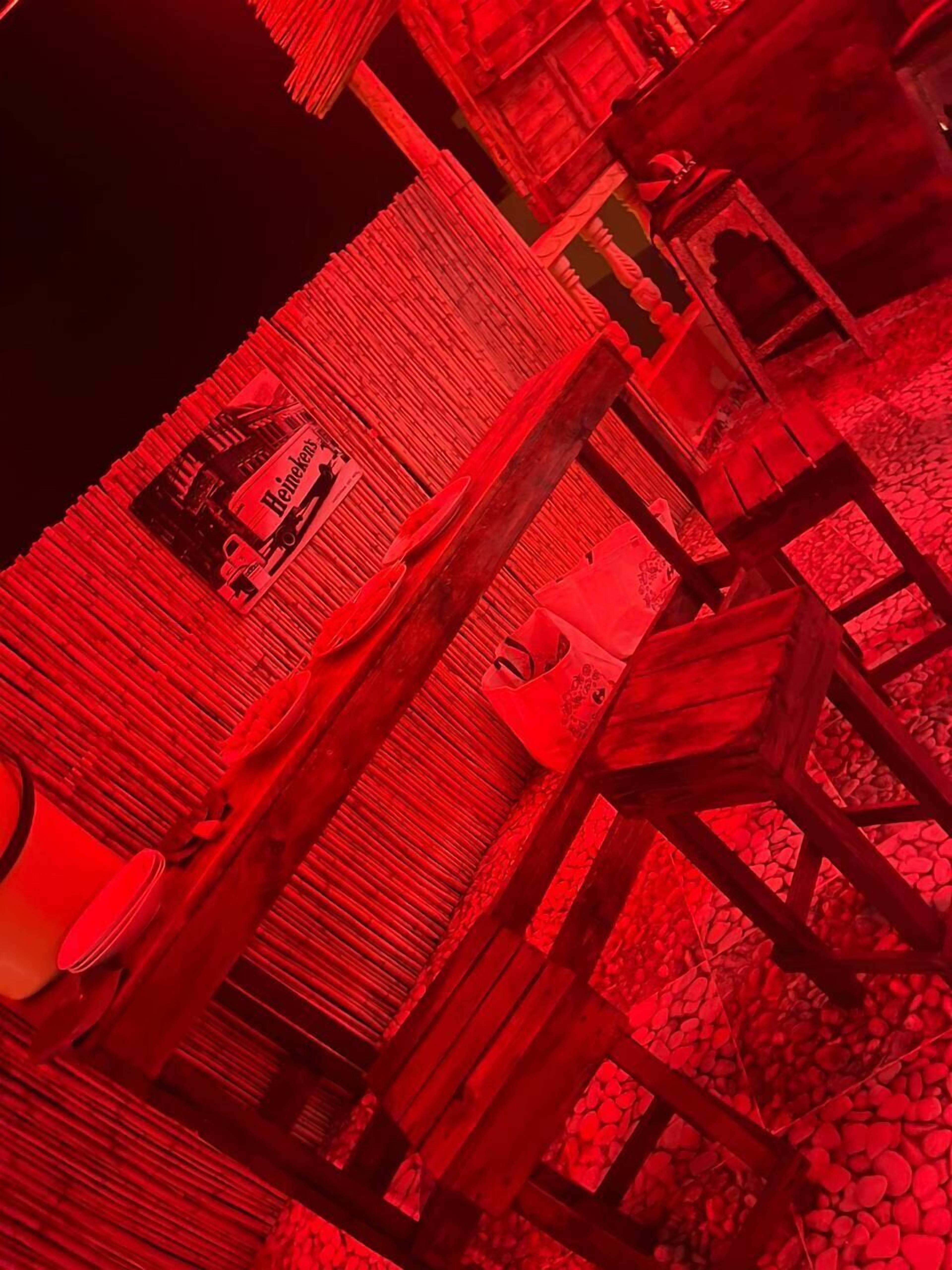 A room with a red hue, featuring wooden furniture and a bed.