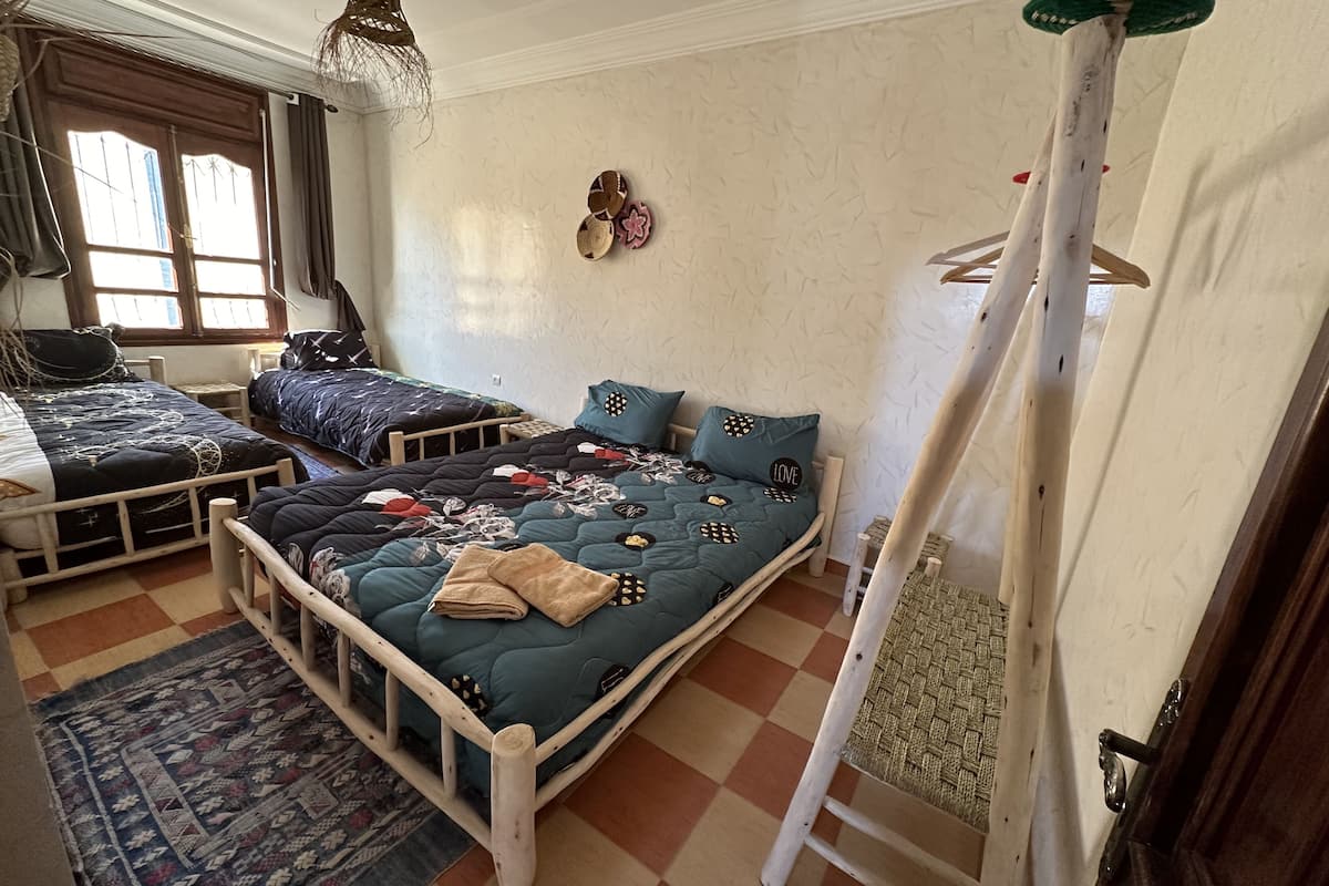 Una habitación con dos camas, un ventanal grande, una lámpara colgante y una escalera.
