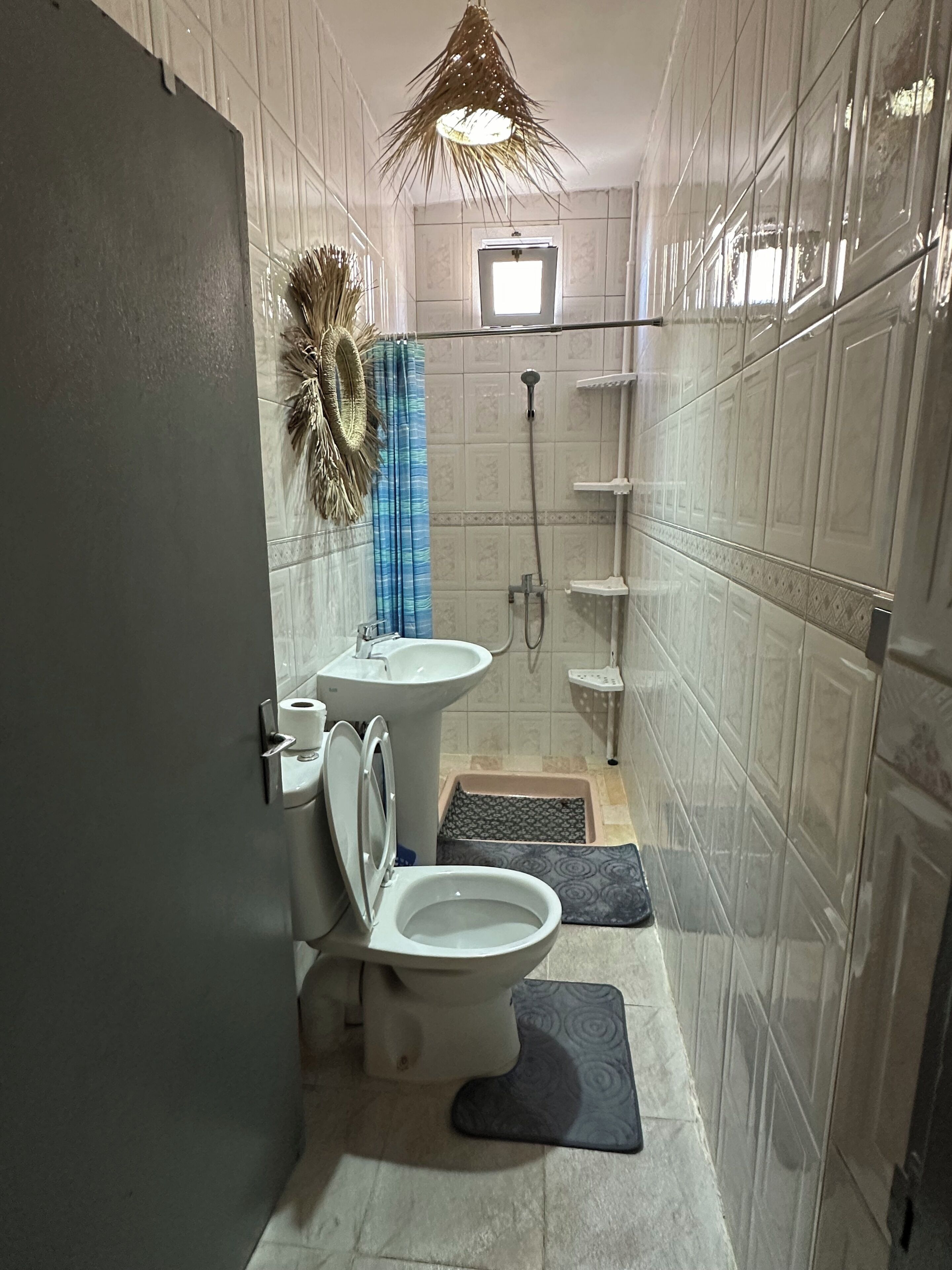A compact bathroom with a toilet, sink, shower, and a small window.