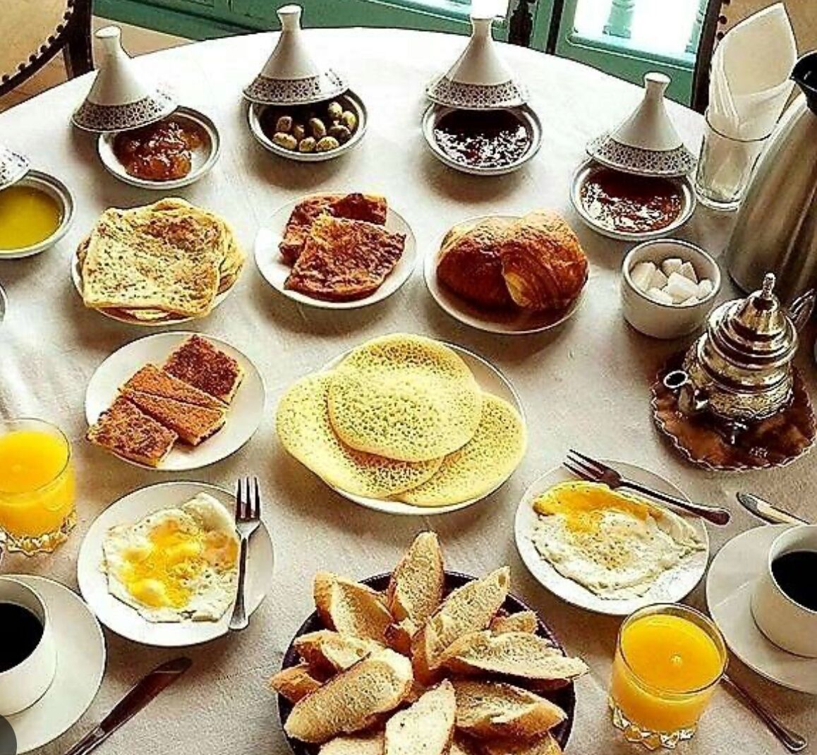 A breakfast setting with various dishes, including bread, eggs, and beverages, arranged on a round table.
