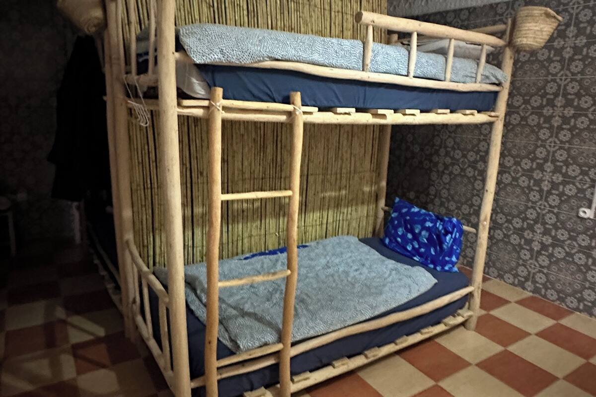 Una cama litera con respaldo trenzado y piso a cuadros.