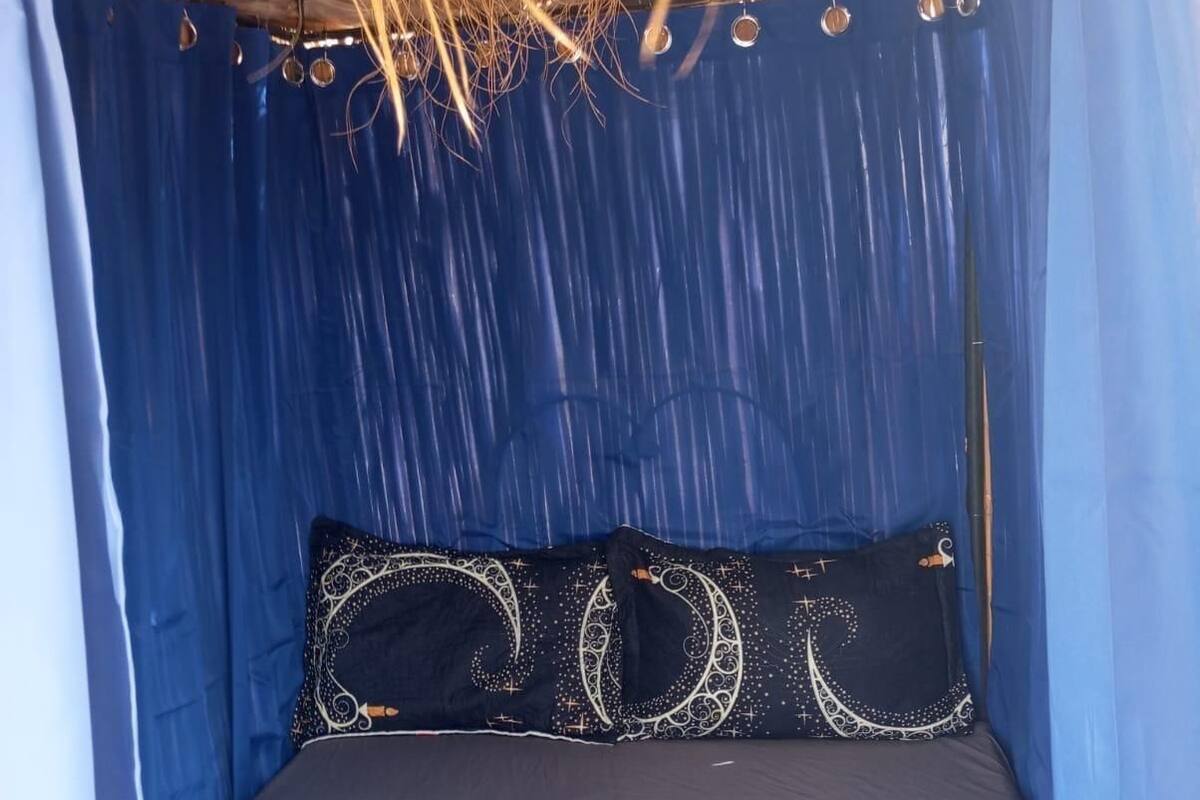 Una habitación con cama, cortinas azules y techo de paja.