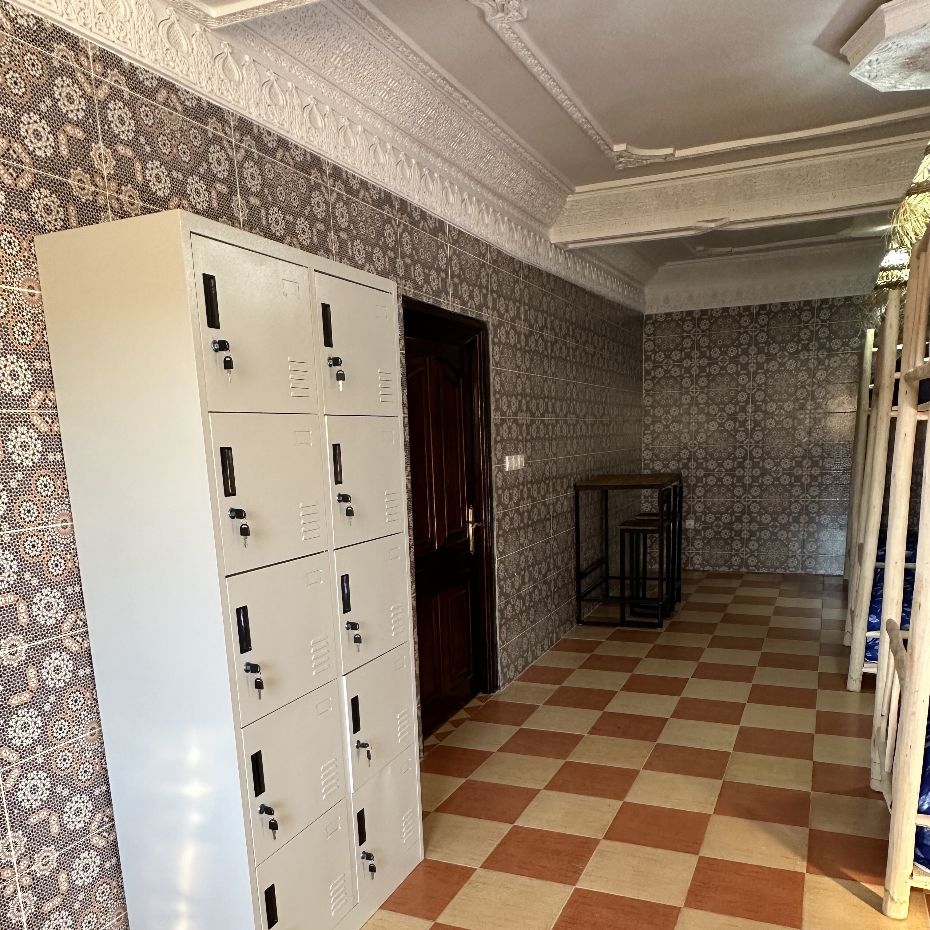 A hallway with patterned wallpaper, a checkered floor, and a row of metal lockers.