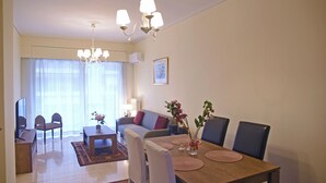 A modern living room with a dining area, featuring a wooden dining table, chairs, a sofa, and a TV. - Athens Faliro Beach Residence, by the city center (Paleo Faliro)