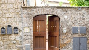 A stone wall with a large wooden double door, mailboxes, and a plaque. - Le Dimore di Borgo Tessile - Feronia (Orvieto)