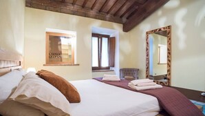 A bedroom with a large bed, a wooden headboard, a mirror with a geometric frame, and a window with curtains. - Le Dimore di Borgo Tessile - Feronia (Orvieto)