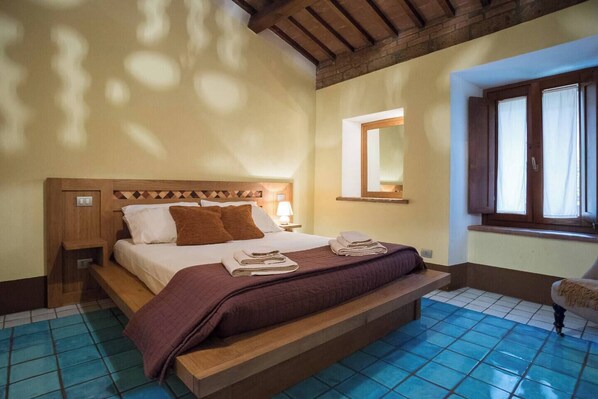 Habitación de hotel con cama de madera, mesita de noche, espejo y ventana con cortinas.