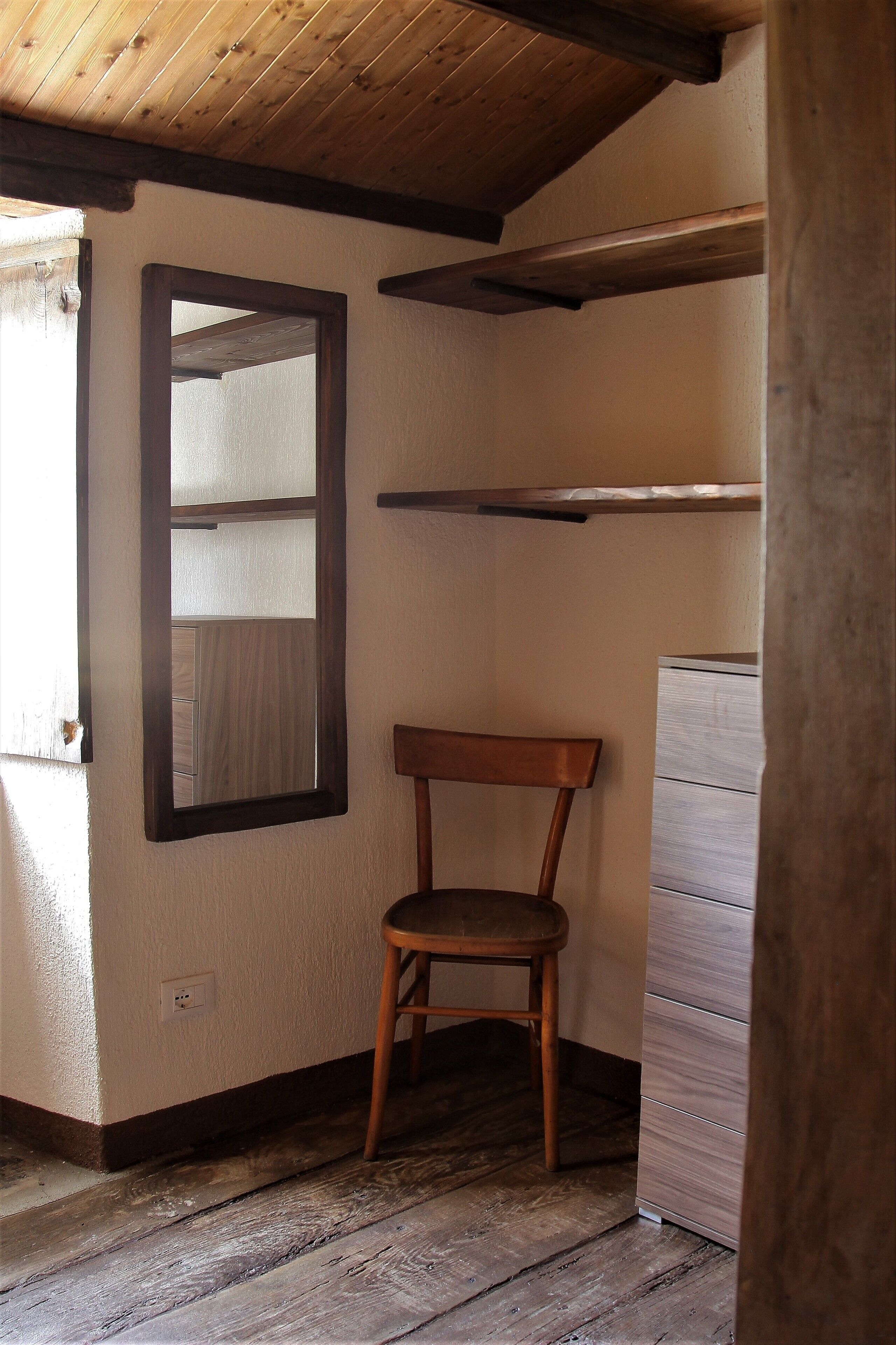 Una stanza con una sedia di legno, uno specchio e un comò in legno.