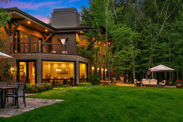 A two-story house with a well-maintained lawn, outdoor seating area, and a large window overlooking the garden. - Villa Fleuve (Ketchum)