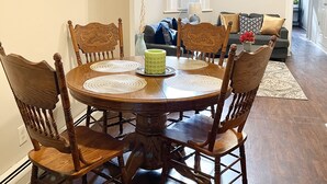 A dining area with a round wooden table and chairs, a vase, and a window with blinds.