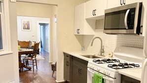 A kitchen with a stove, microwave, sink, and cabinets. There is a dining area with a table and chairs visible in the background.
