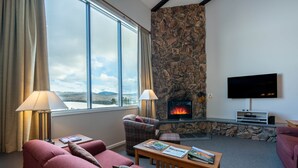 A living room with a stone fireplace, a flat-screen TV, and a sofa with a view of the outdoors.