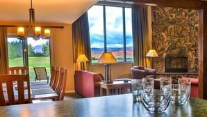 A cozy room with a fireplace, a dining area, and a view of the outdoors. - Marcy Lodge u1 - Magnificent Mountain Views! (Lake Placid)