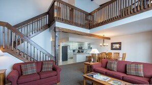 A spacious living area with a wooden staircase, a kitchen in the background, and a red sofa set. - Marcy Lodge u1 - Magnificent Mountain Views! (Lake Placid)