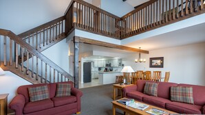 A spacious living area with a wooden staircase, a kitchen in the background, and a red sofa set.