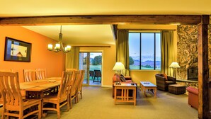 A hotel room with a wooden dining table, chairs, a sofa, a fireplace, and a view of the outdoors. - Colden Lodge u15 - Enjoy Mountain Views (Lake Placid)