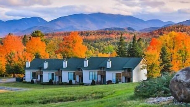 A two-story building with a green roof, surrounded by autumn-colored trees and mountains in the background. - Colden Lodge u15 - Enjoy Mountain Views (Lake Placid)