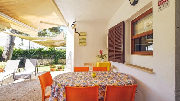 An outdoor dining area with a round table covered by a floral tablecloth, surrounded by orange chairs.