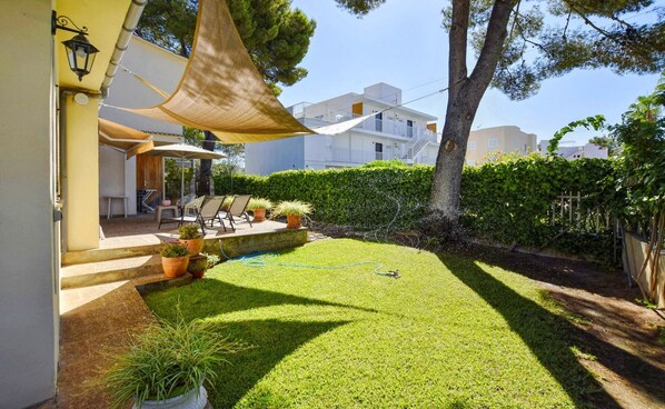 Un jardin bien entretenu, avec une pelouse, un espace extérieur aménagé pour s’asseoir et des plantes en pot.