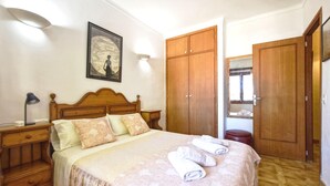 A bedroom with a bed, a nightstand, a lamp, a wardrobe, and a framed picture on the wall.