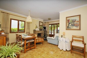 A living room with a dining table, chairs, a sofa, a fireplace, and a painting on the wall. - Holiday Home 'Cora' with Private Terrace, Wi-Fi and Air Conditioning (Alcudia)