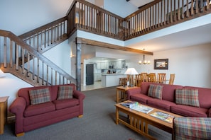 A spacious living area with a wooden staircase, red sofas, a wooden coffee table, and a kitchen in the background.
